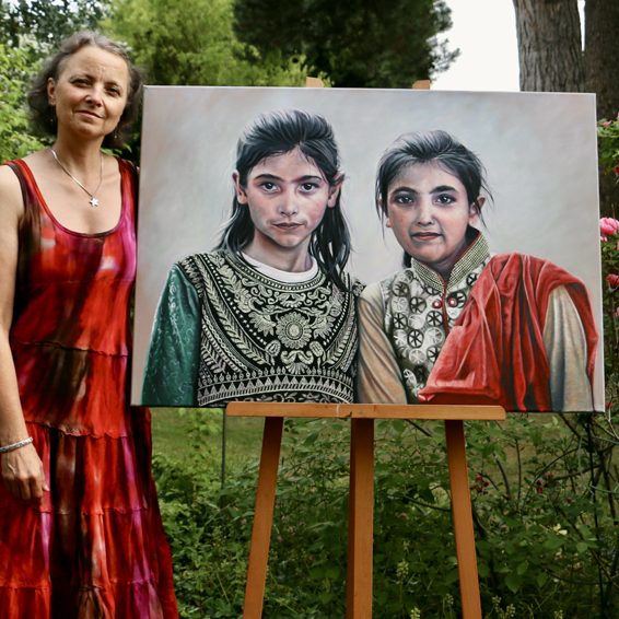 Seona Sommer steht neben einem Ölporträt von zwei afghanischen Mädchen in traditionellen Outfits.